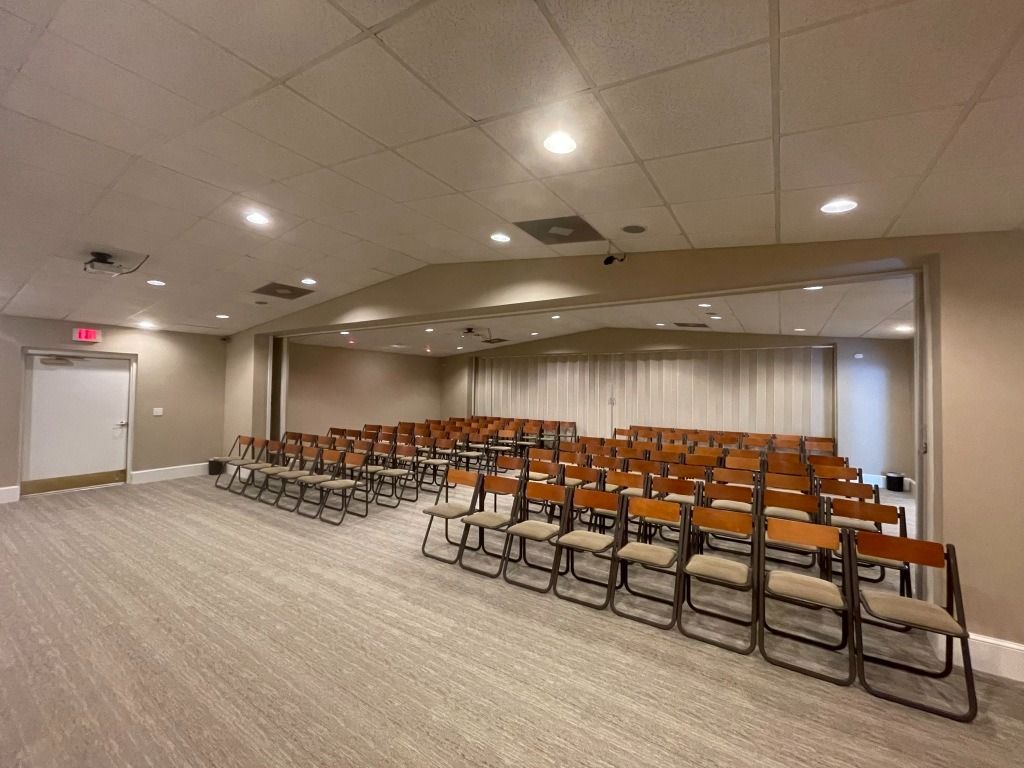 Empty beige meeting room with rows of chairs, neutral carpet, and a white ceiling.