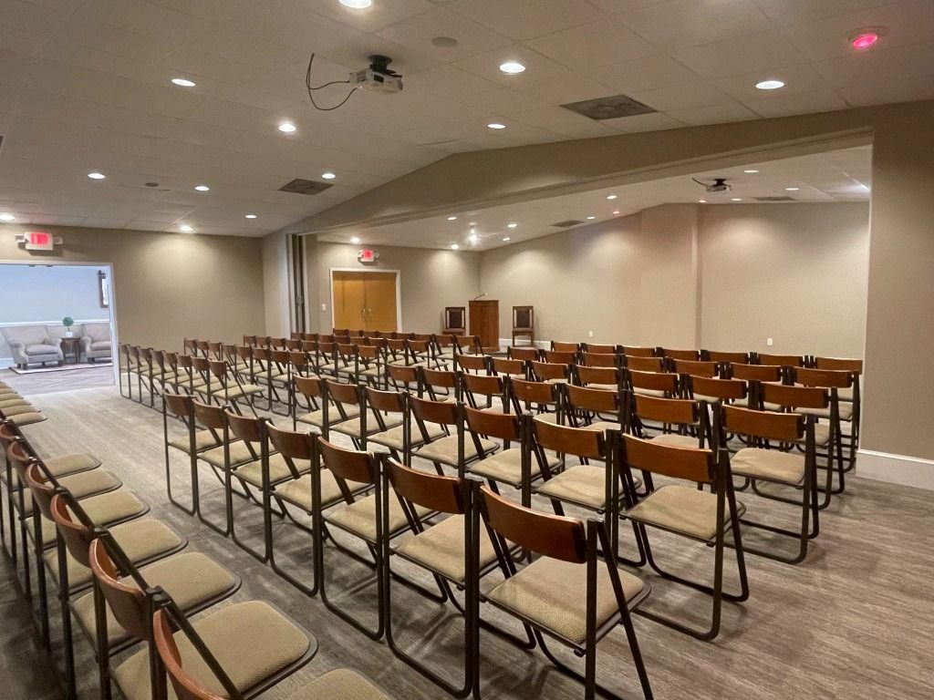 Empty auditorium with rows of chairs, neutral walls, and a projector on the ceiling.