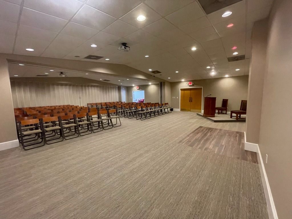 Empty auditorium with rows of chairs, a podium, and a wooden floor area.