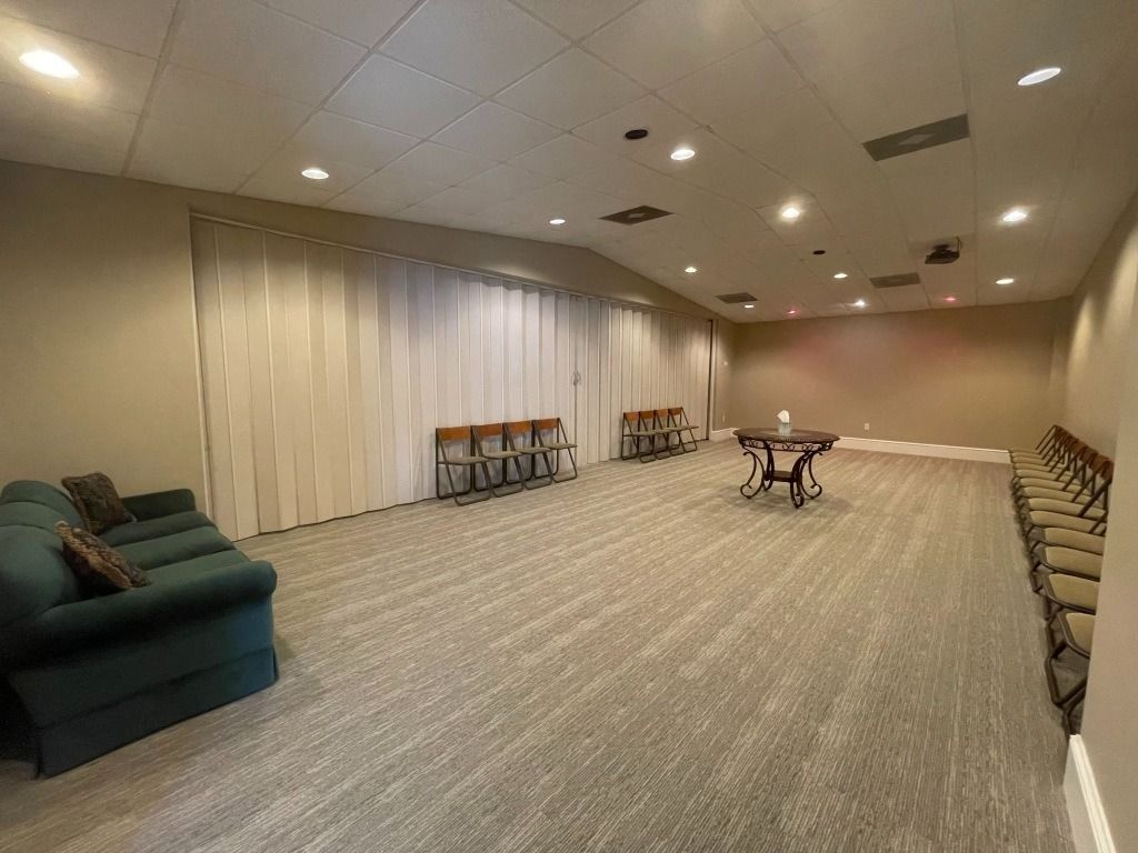 Empty room with carpet, chairs, sofa, and a small table. Neutral colors and overhead lighting.