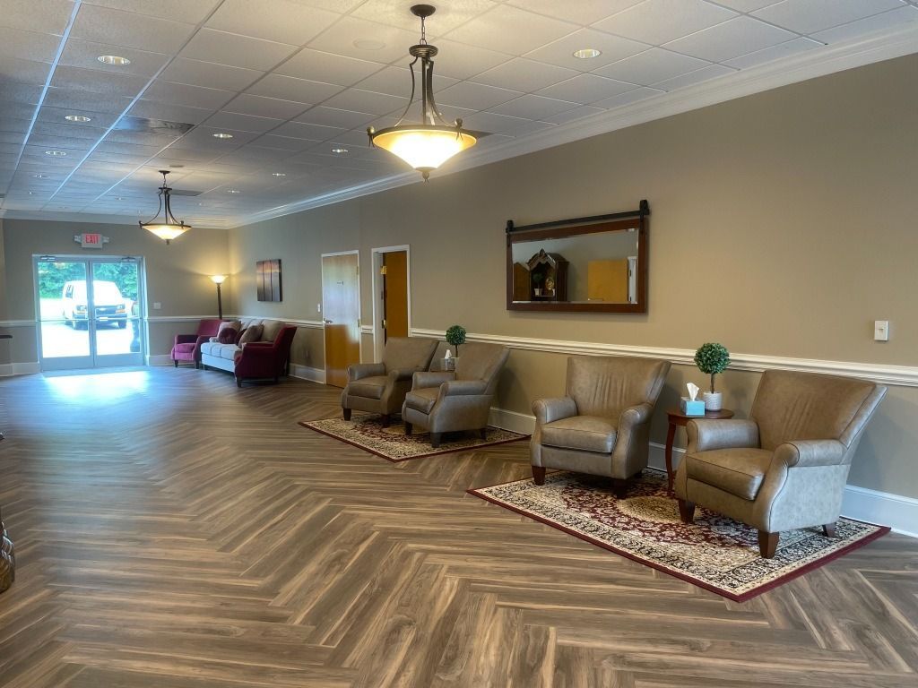 Lounge area with neutral walls, herringbone floor, comfortable chairs, and decorative mirrors; a door leads outside.