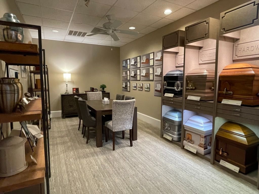 Funeral home display room with caskets on shelves, table with chairs, and decorative items.