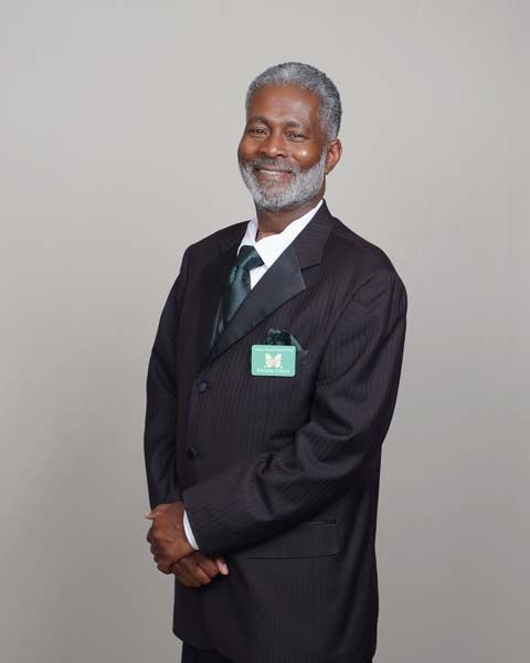Man in black suit with green tie and pocket square, smiling, name tag visible.