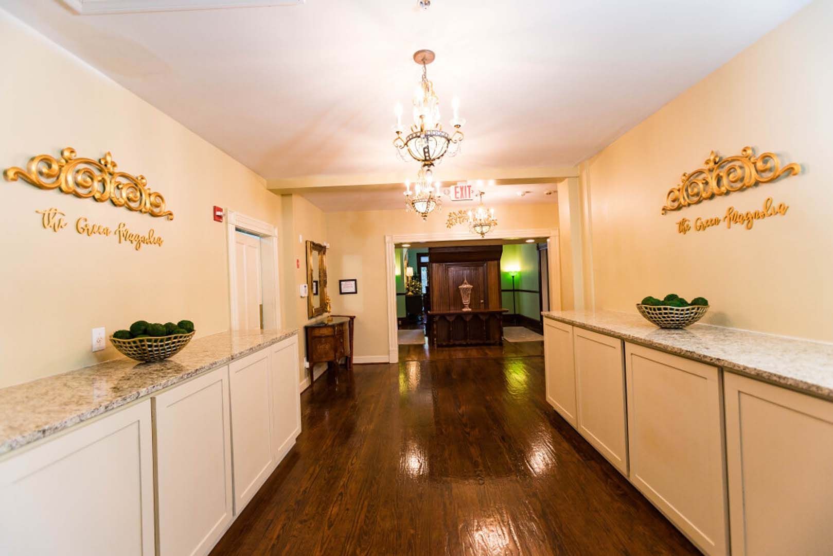 Long hallway with chandeliers, cream-colored walls, white cabinets, and dark wood floor.