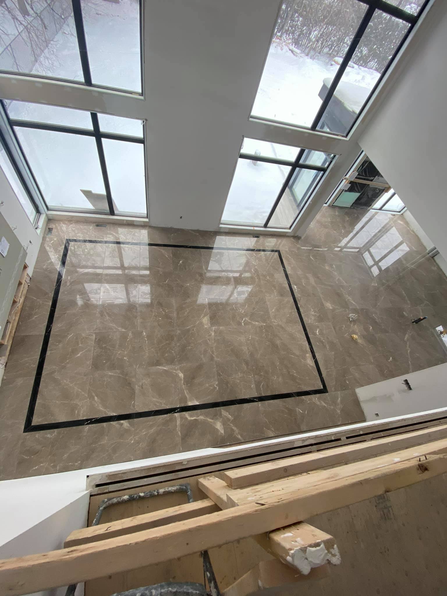Modern lobby with glossy marble floor, large windows, and a rectangular floor opening under construction