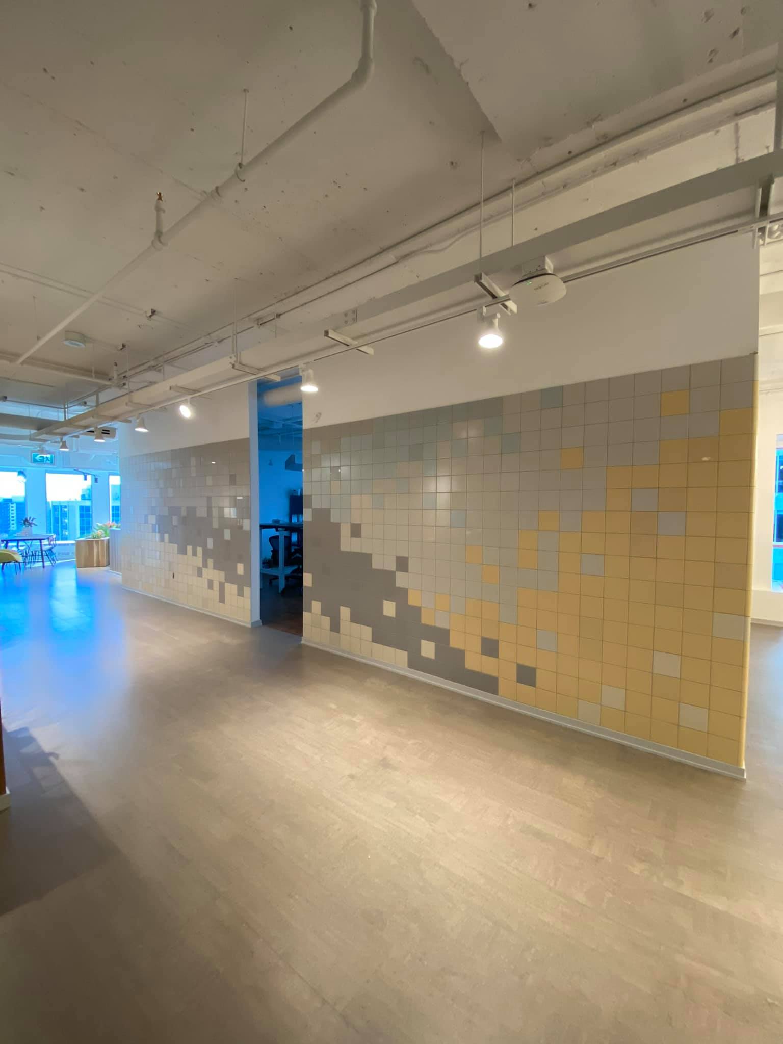 Empty indoor hallway with wood floors, recessed lights, and a long wall of beige square panels