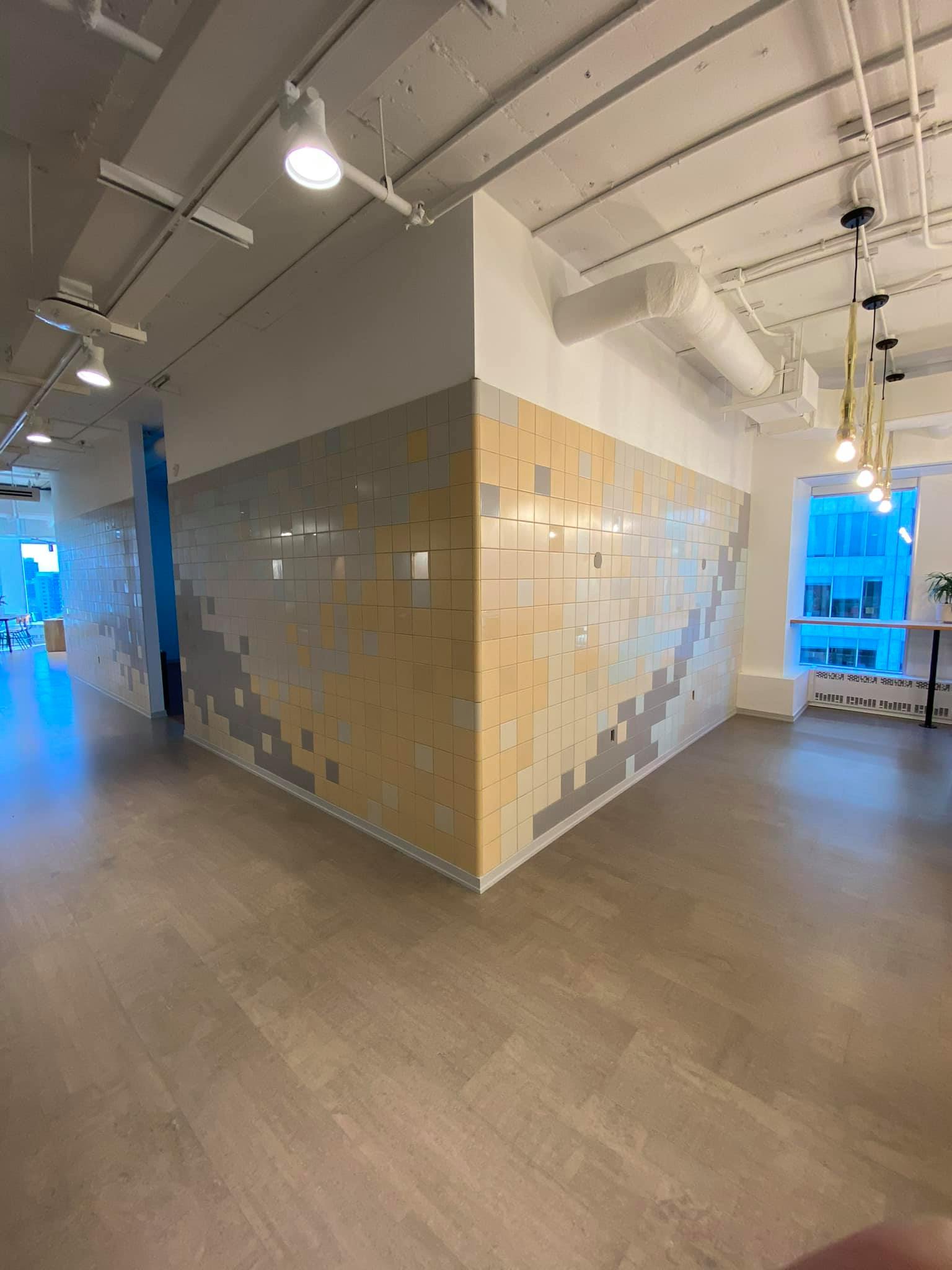 Office hallway with tiled corner wall, wood floor, ceiling lights, and blue-lit windows.