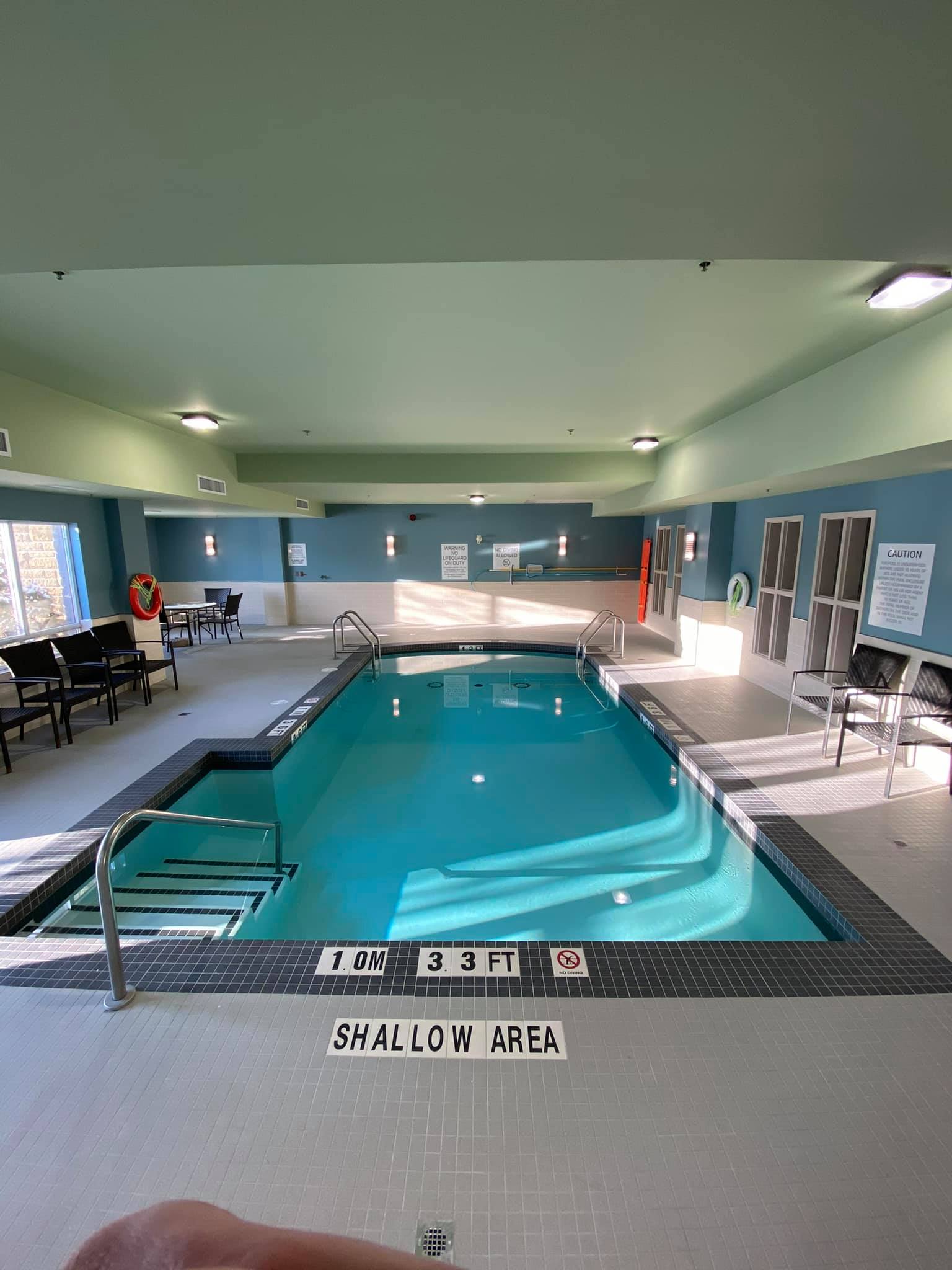 Indoor swimming pool with turquoise water, metal handrails, and lounge chairs in a bright room