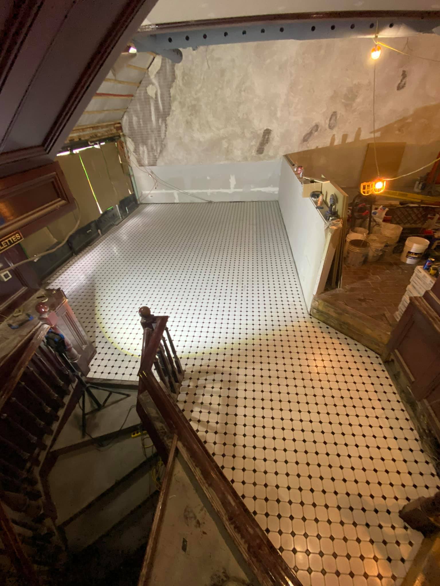 Abandoned indoor space with a large white perforated floor panel, worn plaster wall, and dim lighting.