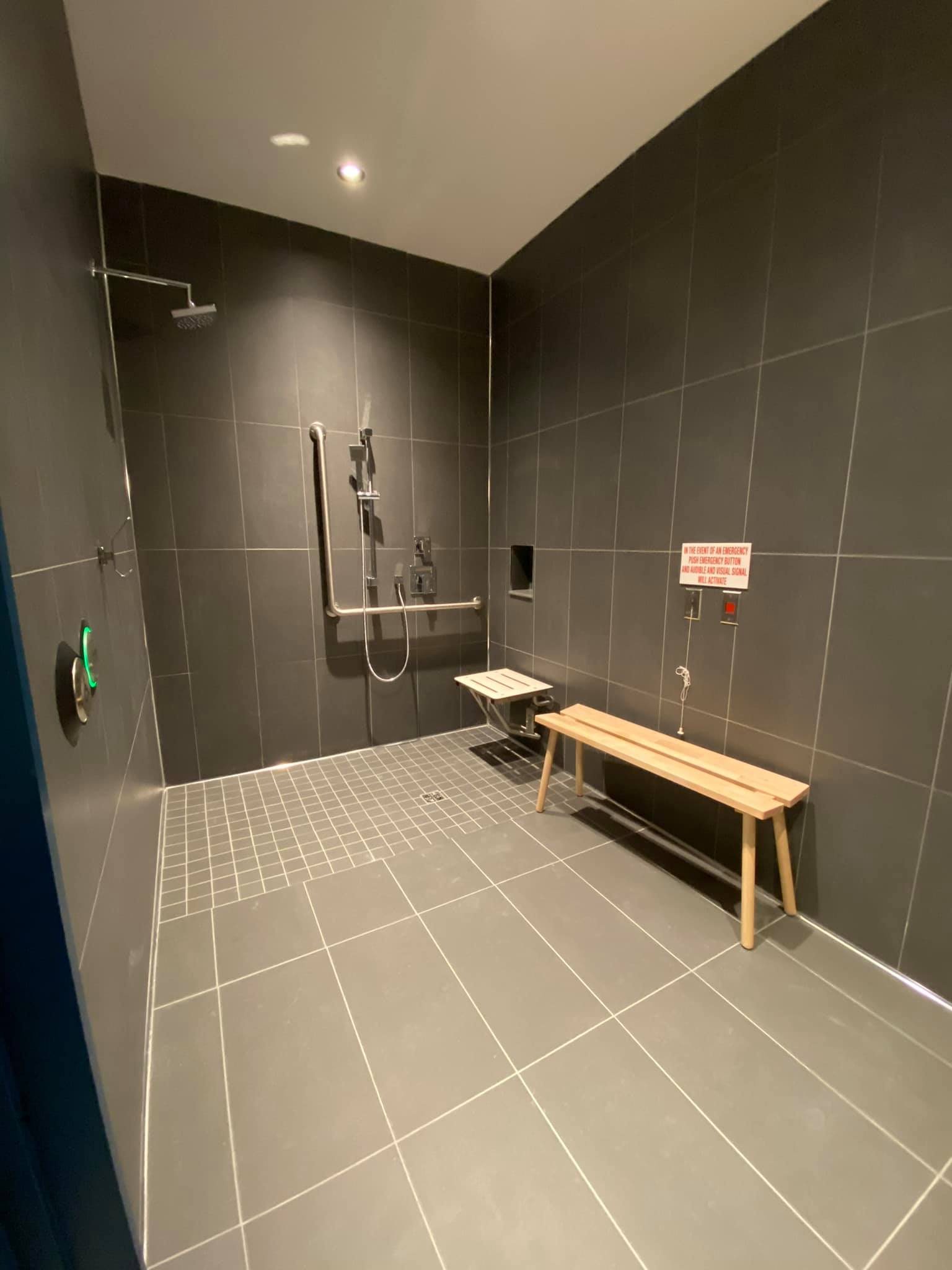 Modern shower room with dark tiled walls, bench, handrails, and accessible shower fixtures.