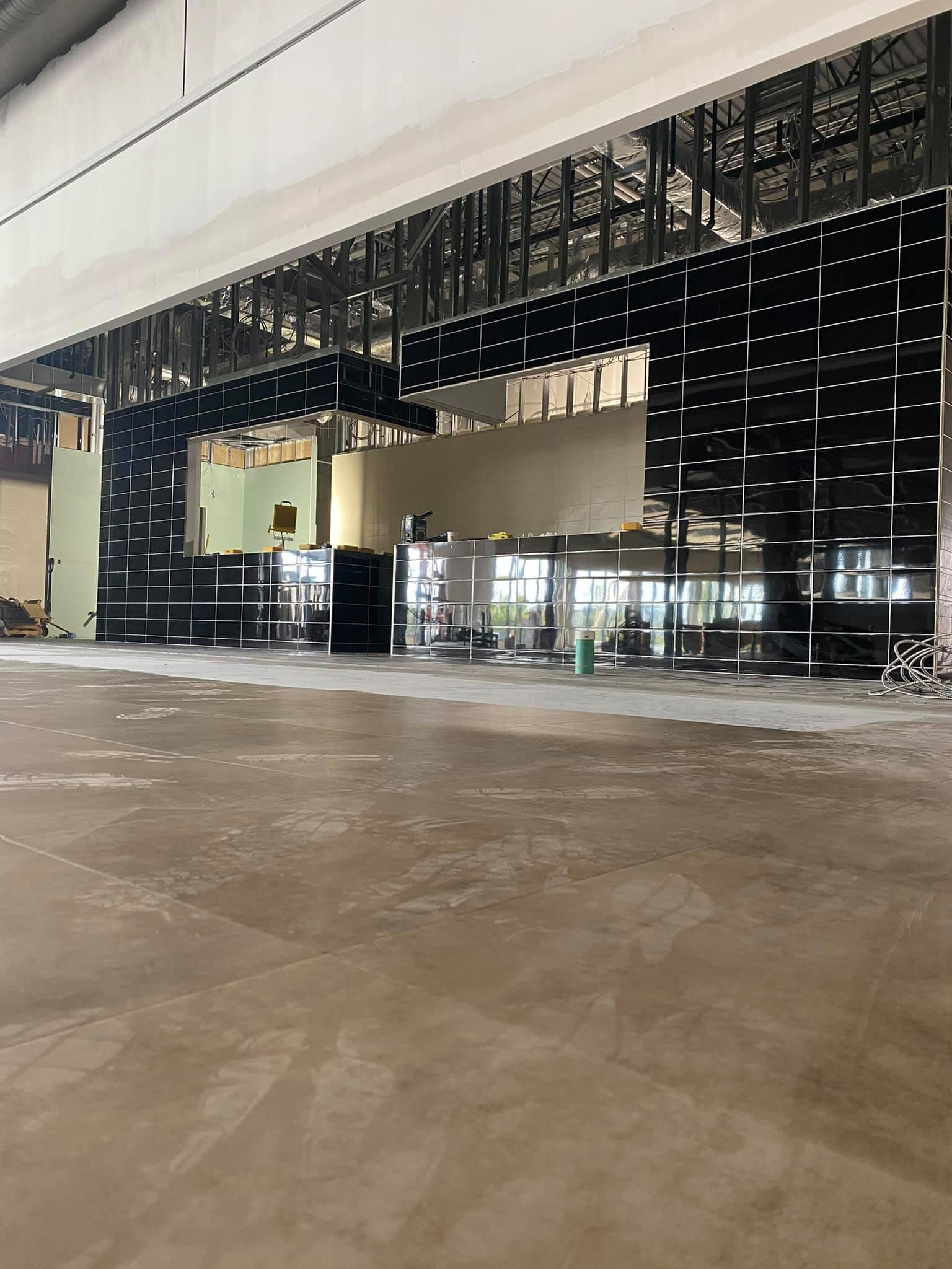 Empty unfinished indoor hall with exposed framing, glass storefronts, and a bare concrete floor.