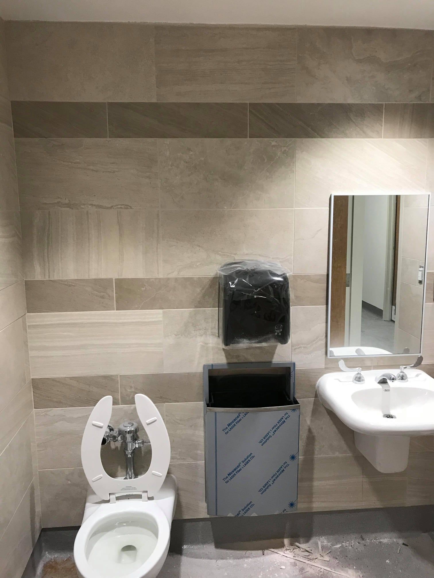 Accessible restroom with toilet, paper dispenser, sink, and mirror against tiled walls