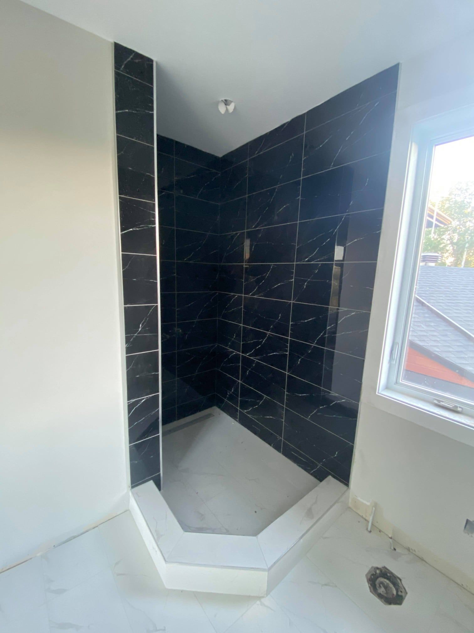 Tiled shower nook with dark walls, a white shower pan, and a nearby window.