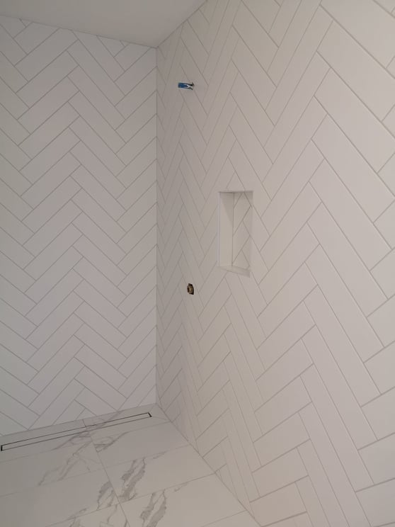 Empty white-tiled shower stall with chevron wall tiles and a recessed niche.
