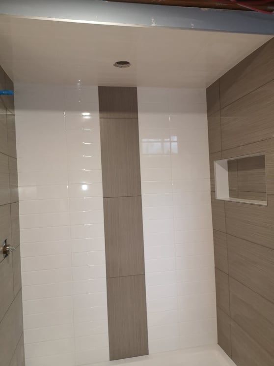 Tiled bathroom shower with white and beige walls and a built-in shelf niche