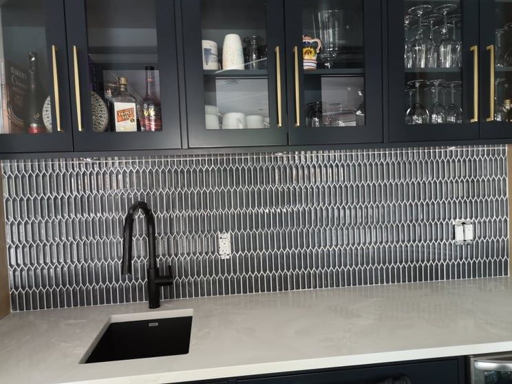 Modern kitchen with dark cabinets, gray mosaic backsplash, black sink and faucet, and light countertop