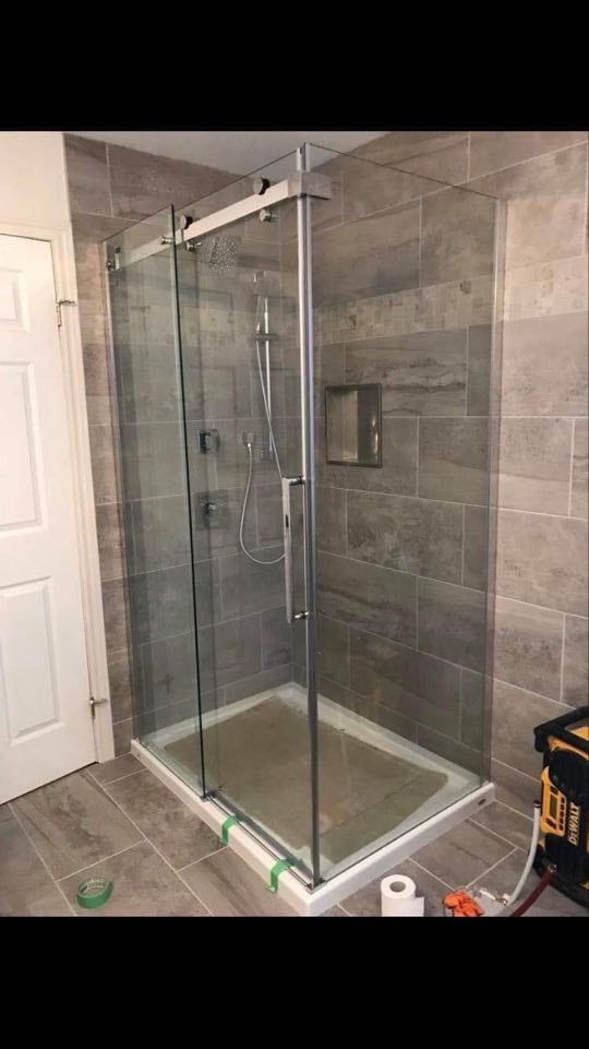 Glass-enclosed corner shower with chrome fixtures in a tiled bathroom