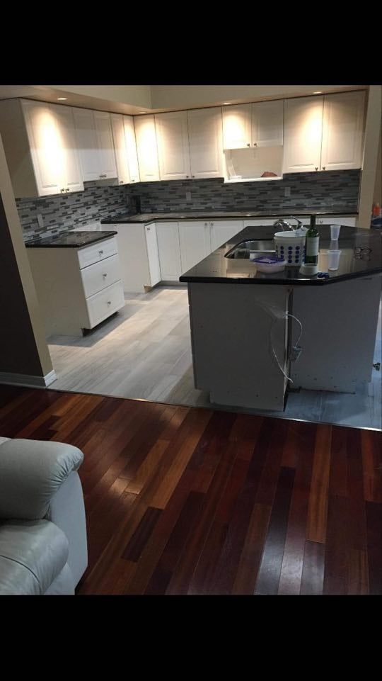 Modern kitchen with white cabinets, dark granite island, and polished wood floor.