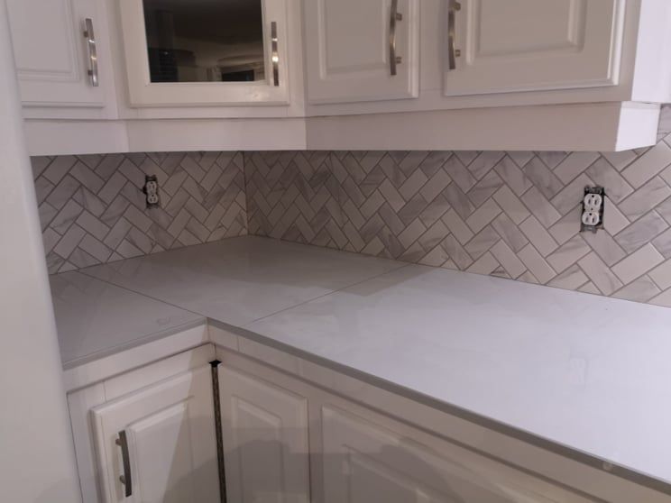 White kitchen corner with herringbone tile backsplash, countertop, and cabinets