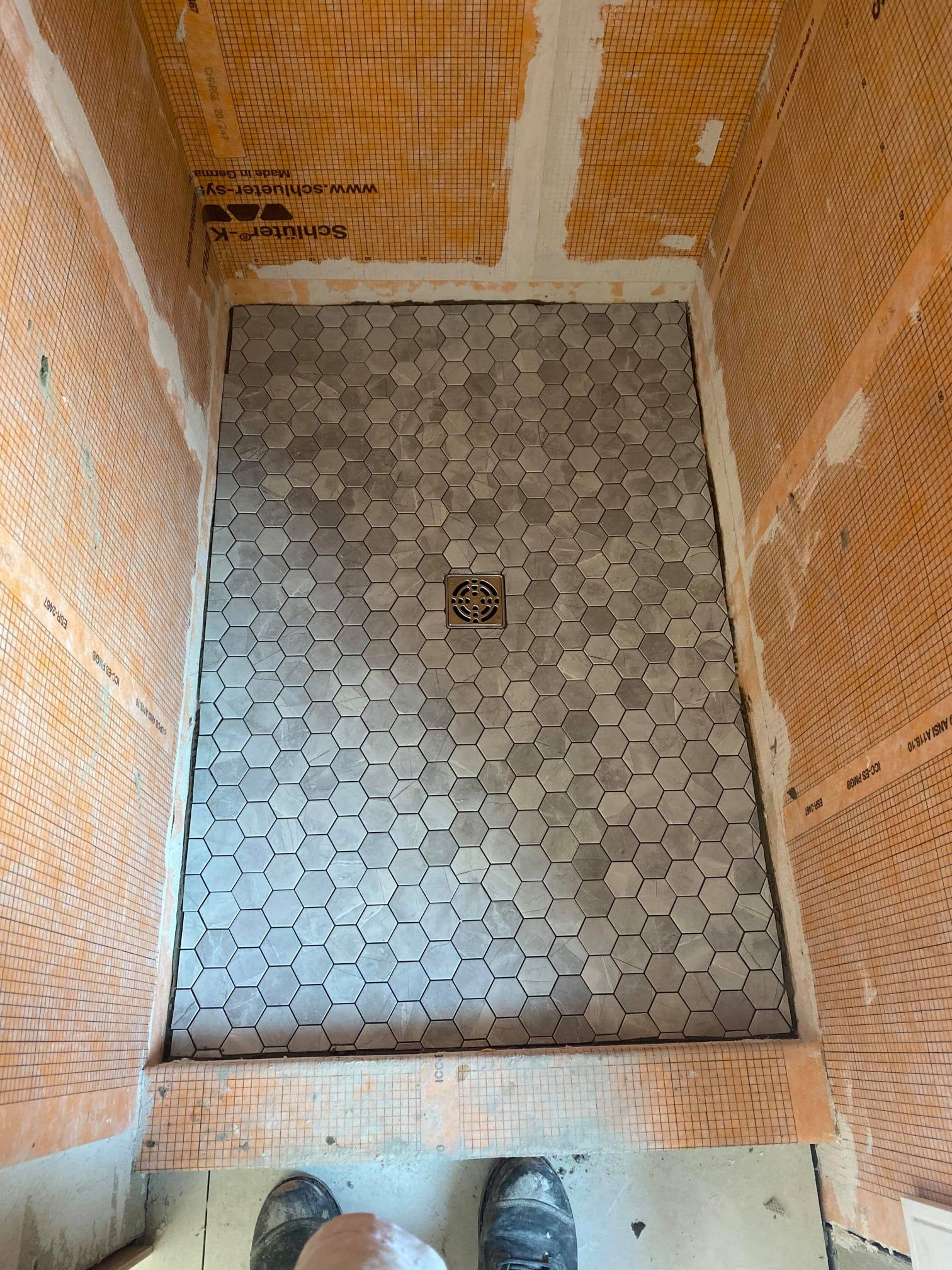 Small tiled shower stall with orange mesh walls and a square drain in the center.