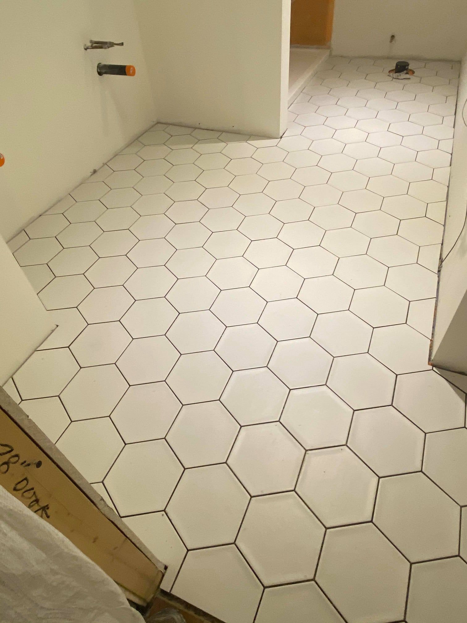 Empty tiled room with white hexagonal floor tiles and a doorway at the back.