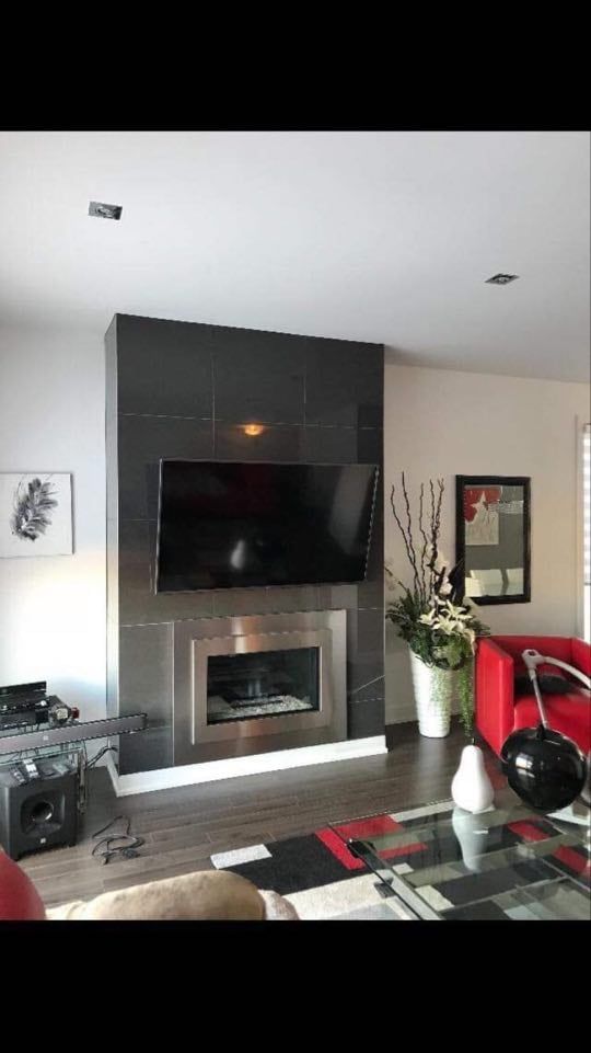 Modern living room with a wall-mounted TV above a fireplace, gray accent wall, and red chair