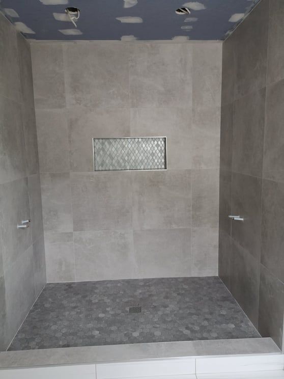 Tiled shower stall with gray walls, dark floor, and a small glass block window.