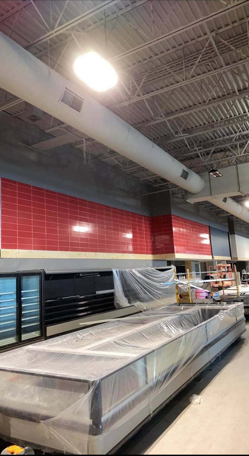 Empty grocery store aisle with refrigerated display cases and red tiled wall under industrial lighting