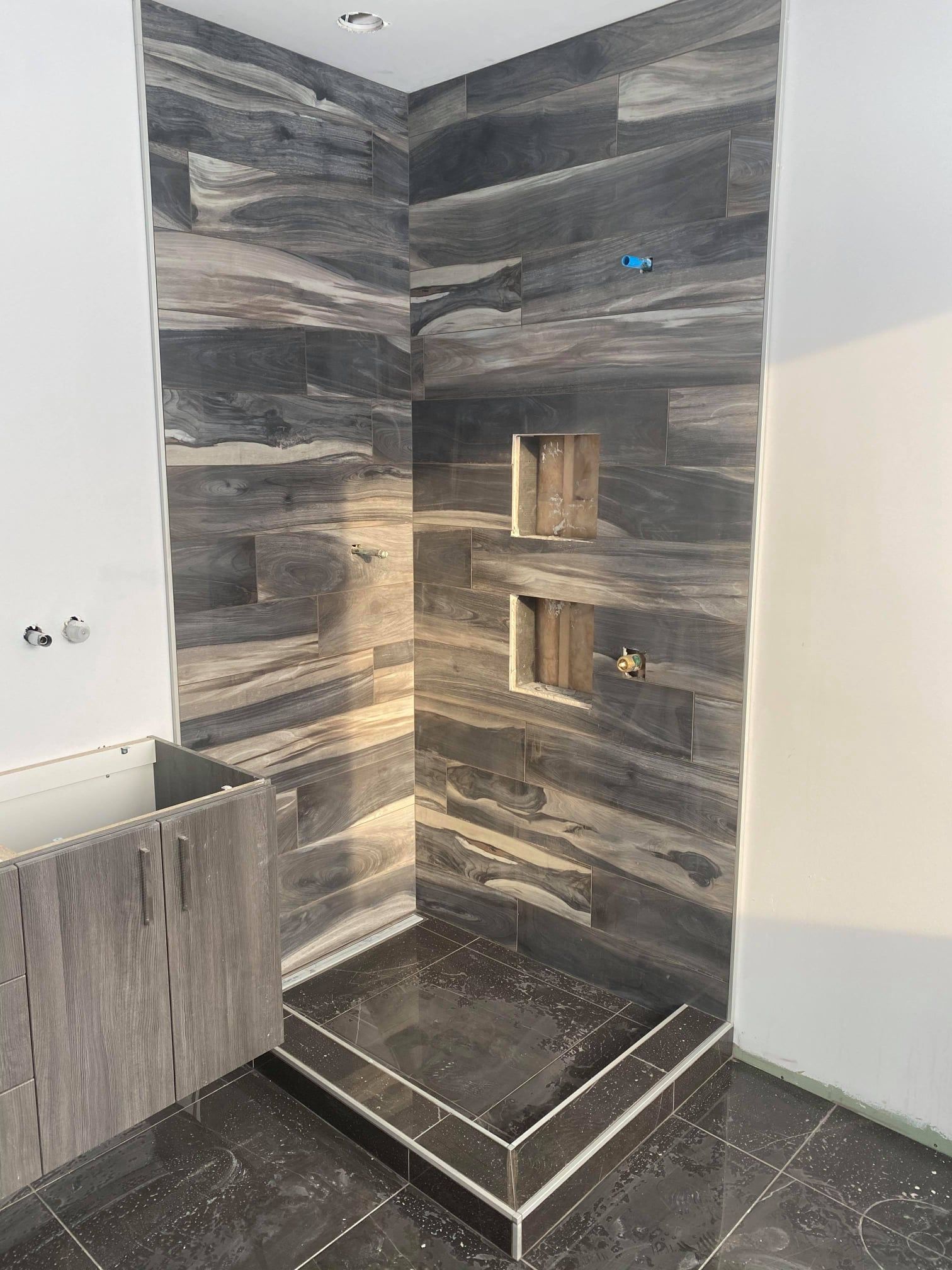 Modern tiled walk-in shower corner with gray stone walls, built-in niches, and a low black shower tray