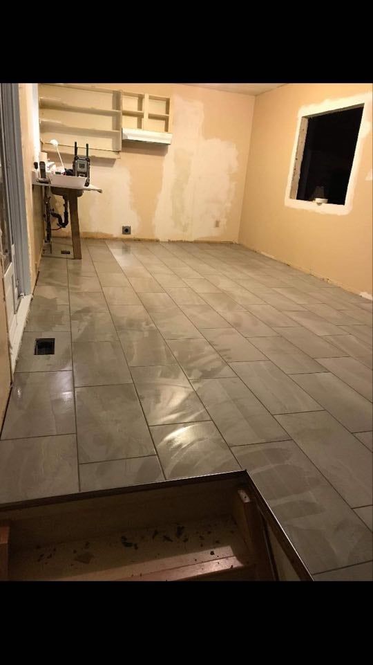 Empty tiled room with beige walls, a window opening, and a small counter in the back.