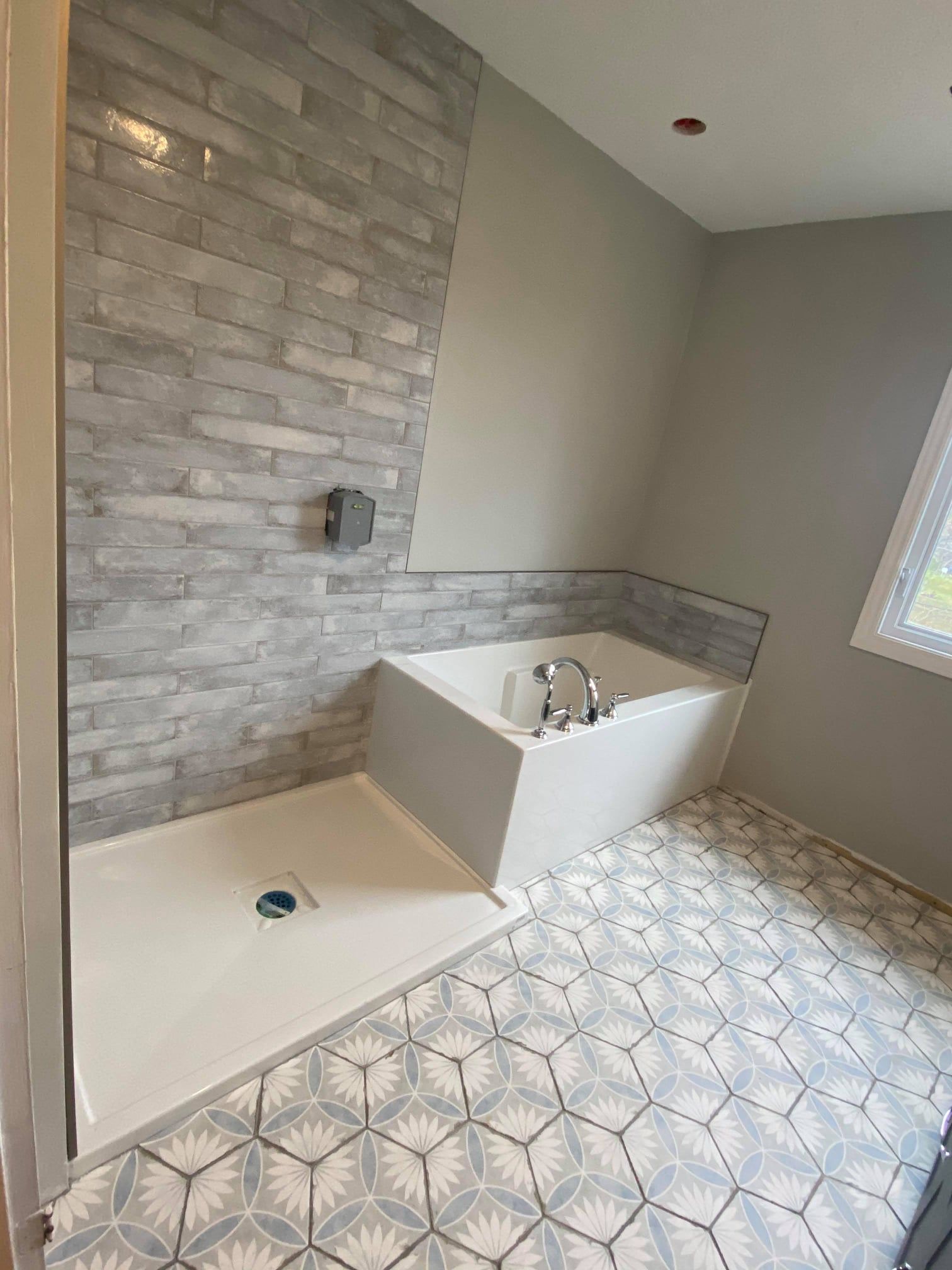 Empty bathroom with tiled floor, stone accent wall, and a freestanding tub near a window.