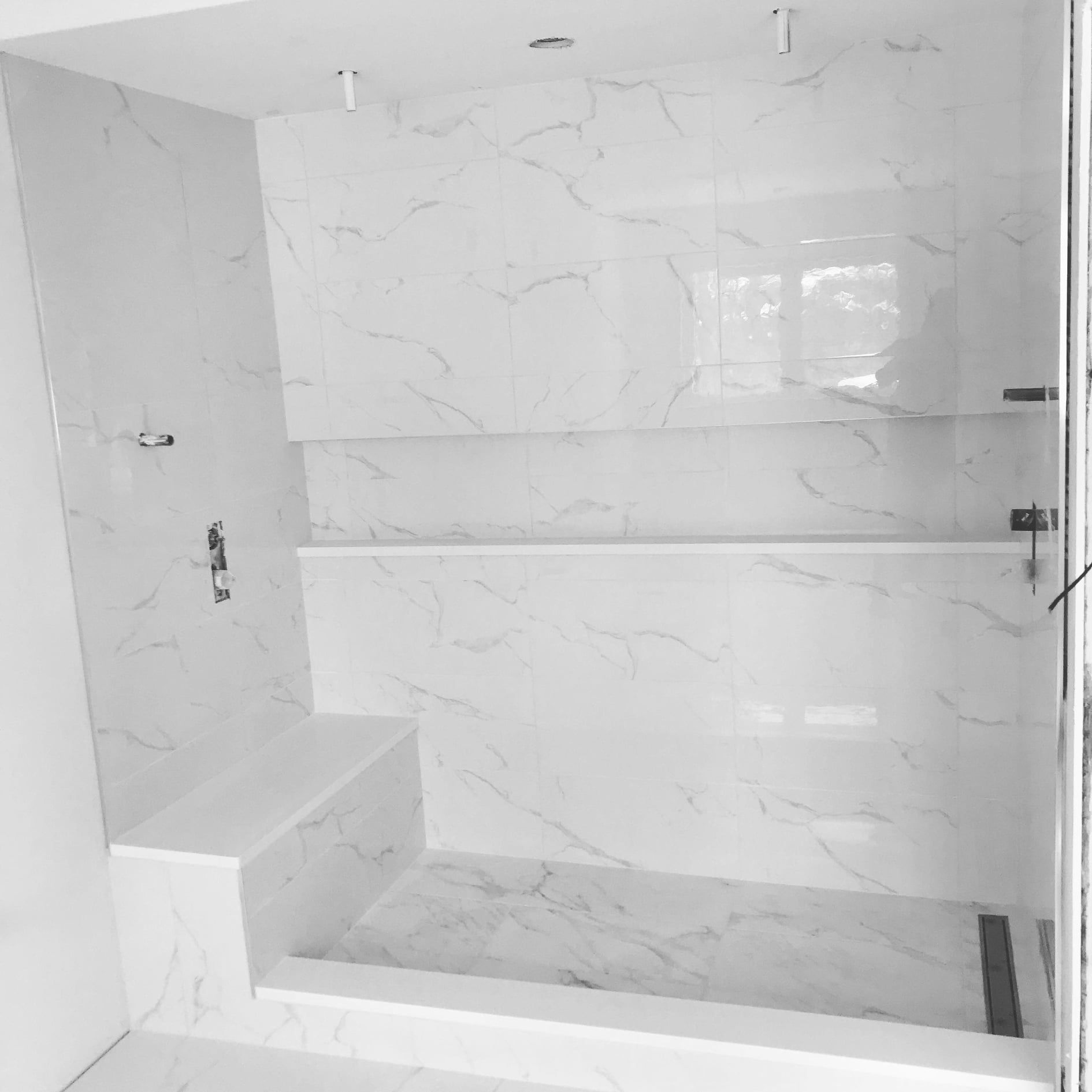 Modern white tiled walk-in shower with built-in bench and glass door