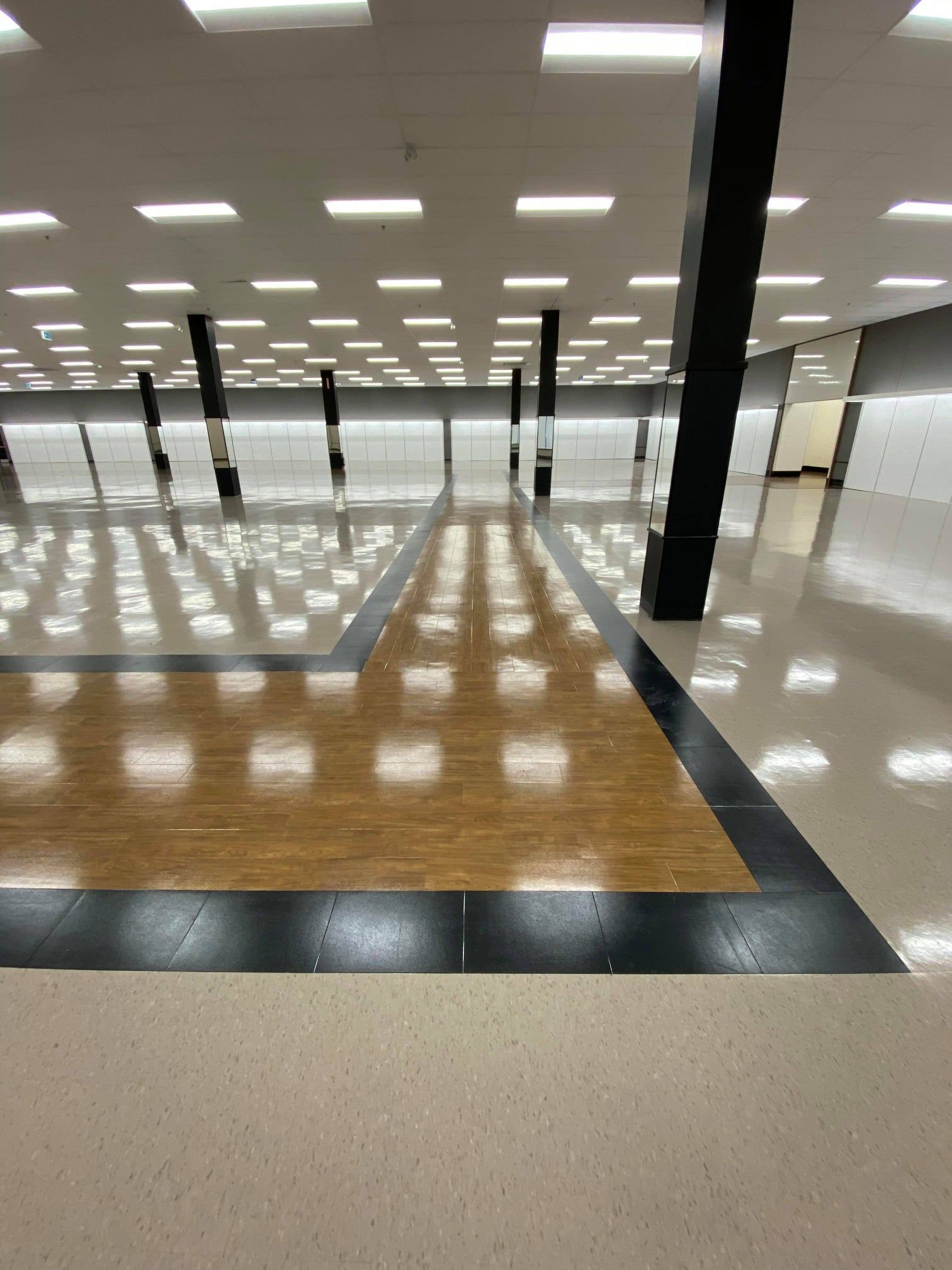 Empty room with glossy wood floor, white ceiling lights, and black columns in a large indoor hall
