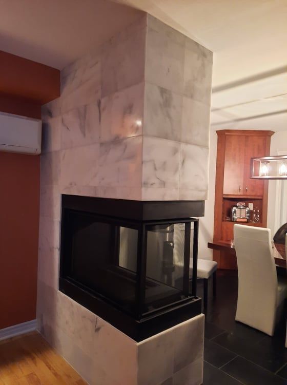 Corner marble fireplace with glass front in a dining room, with a chair and cabinet in the background