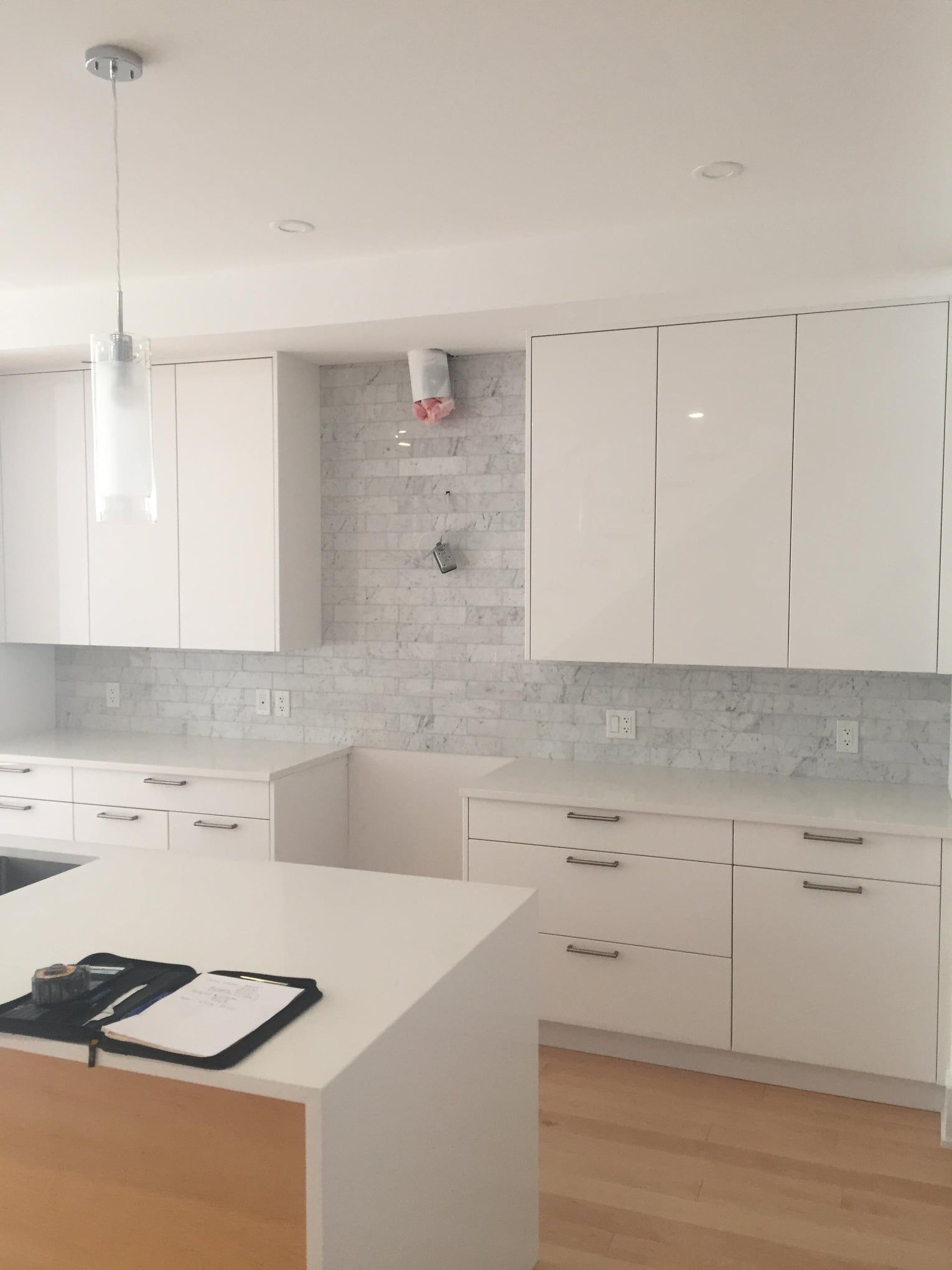 Bright modern kitchen with white cabinets, marble backsplash, island, and light wood floor