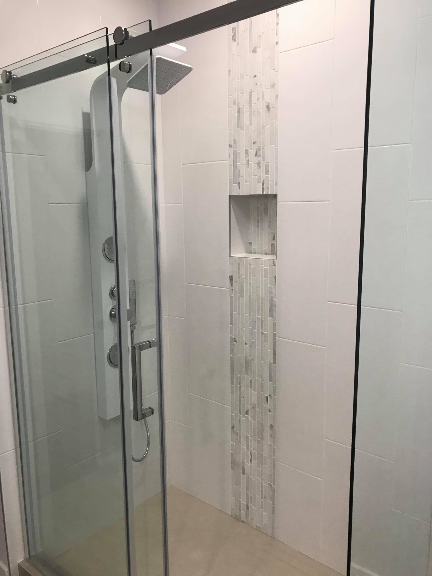 Glass shower enclosure with a central wall niche and water running down the tiled shower wall.