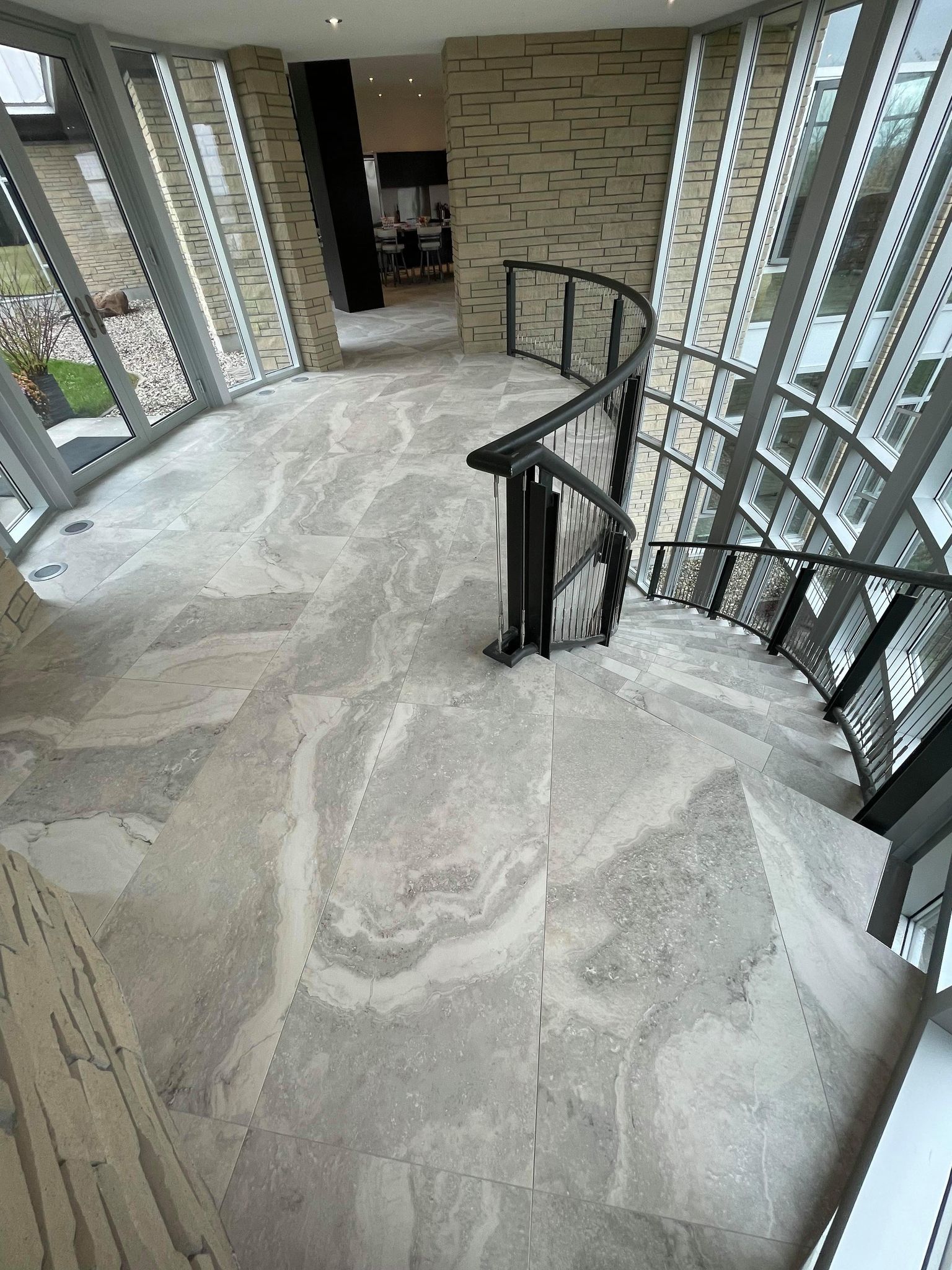 Curved stairwell with glass railing and patterned stone floor in a modern building lobby.