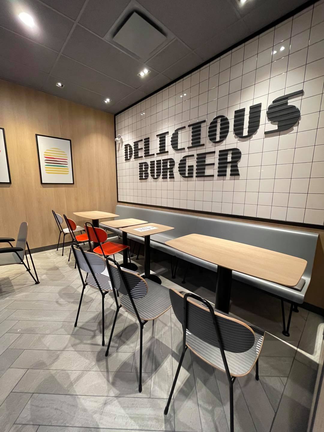 Empty burger restaurant seating with gray tile walls and “DELICIOUS BURGER” sign on the back wall