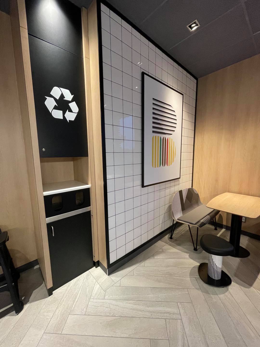Modern café seating area with black-and-wood walls, recycle symbol, table, chairs, and wall art.