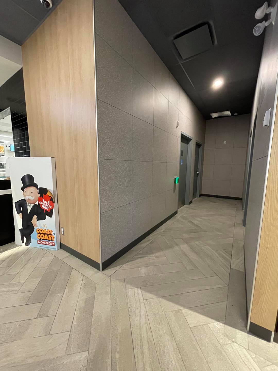 Modern hallway with gray tiled walls, wood paneling, and a poster stand near the corner.