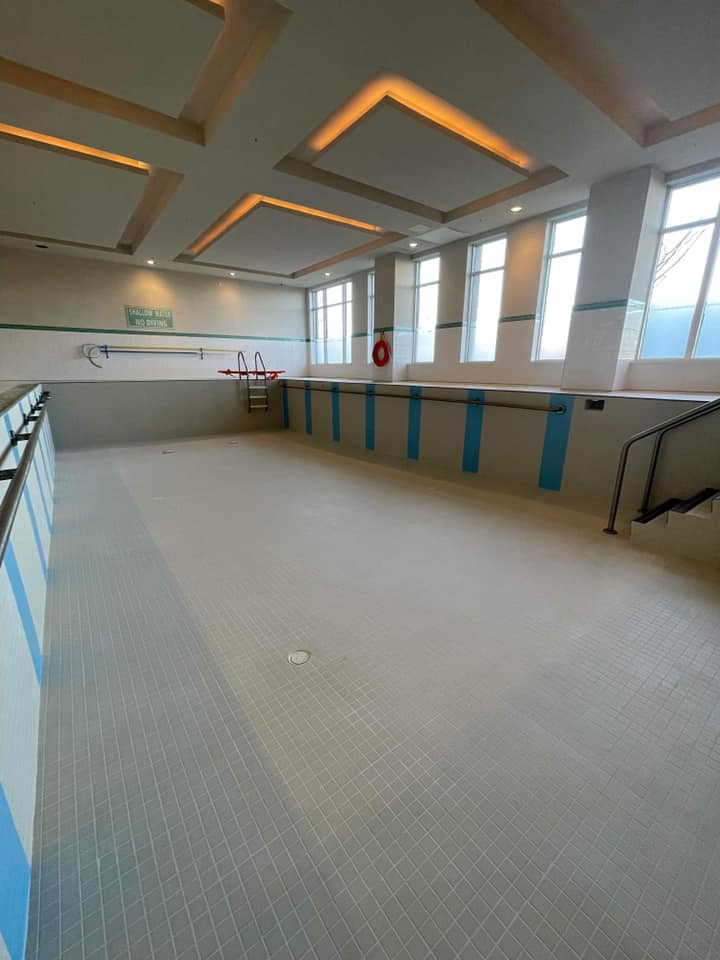 Indoor pool with empty lanes, blue railings, and large windows letting in natural light