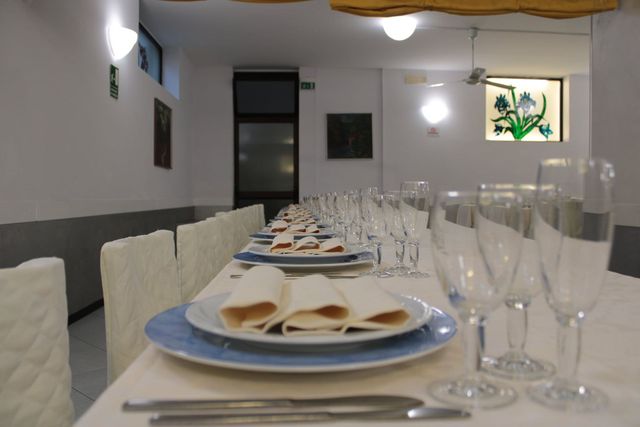 Tavolo da pranzo apparecchiato in una stretta sala da banchetto con sedie bianche e bicchieri.