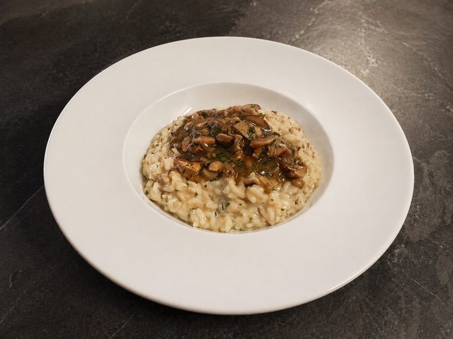 Risotto su un piatto bianco condito con salsa ai funghi su un tavolo scuro