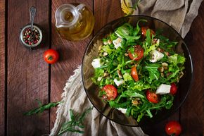 Insalata verde fresca con pomodori e formaggio su un tavolo scuro, con olio d'oliva ed erbe aromatiche a portata di mano.