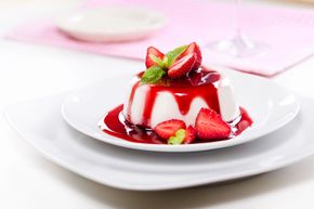 Dessert con fragole e salsa rossa su un piatto bianco con sfondo rosa.