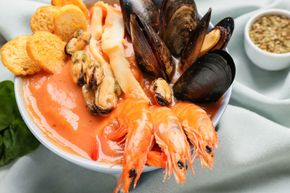 Piatto di frutti di mare con gamberi, cozze, pesce, patatine fritte e salsa per intingere, servito su un piatto bianco.