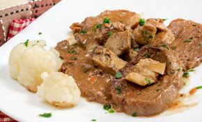 Piatto di spezzatino di carne cremoso e marrone con cimette di cavolfiore su un piatto bianco.