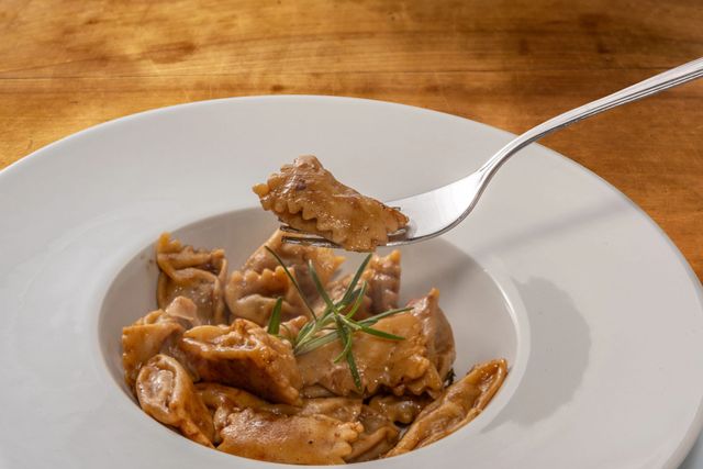 Pasta cremosa in una ciotola bianca, con una forchetta che solleva un pezzo sopra un tavolo di legno.