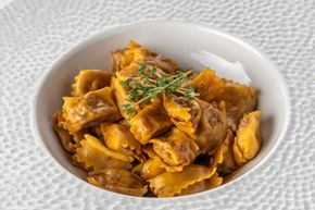 Ciotola di pasta arancione o pezzi di pollo guarniti con erbe aromatiche su una superficie bianca ruvida