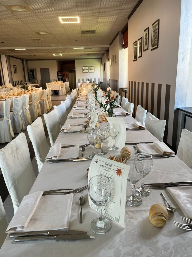 Elegante sala per banchetti allestita con lunghi tavoli apparecchiati con tovaglie bianche, tovaglioli piegati, bicchieri e sedie lungo il corridoio.